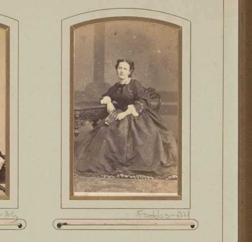 Portrait of a woman, seated at a table with a photo album in her hand