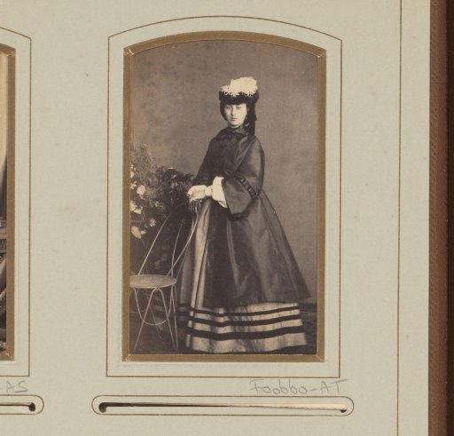 Portrait of a standing woman with coat and hat by a garden chair