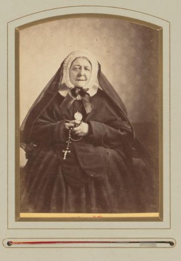 Portrait of a seated religious woman in black, with cornet cap and rosary