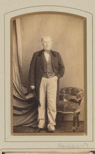 Portrait of a man standing by a chair, with hat in hand