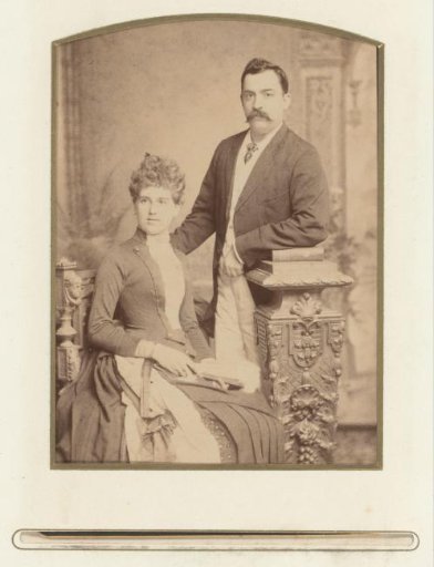 Portrait of a sitting woman with a fan and a standing man leaning on a pillar