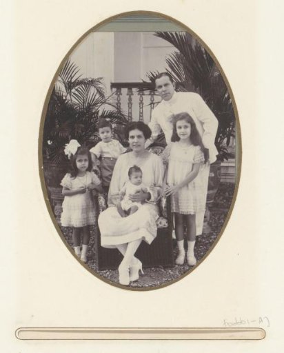Group portrait of a man, a woman and four children on a courtyard in front of a balcony