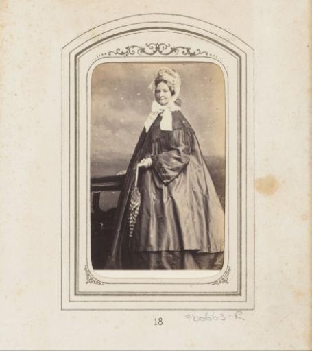 Portrait of a standing woman with a white cap with ribbons and an umbrella