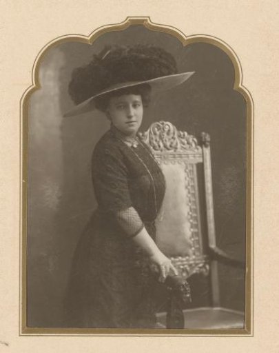 Portrait of a standing woman with a large hat by a chair
