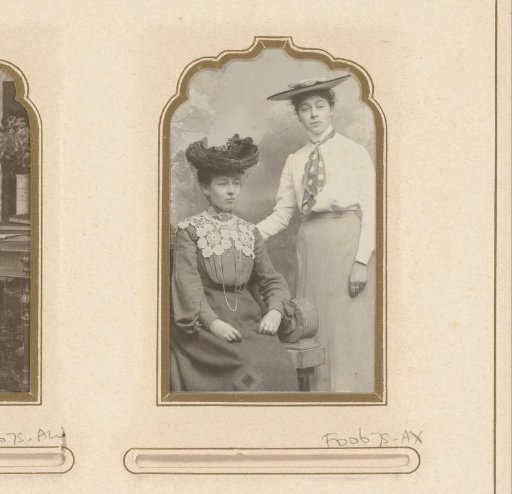 Portrait of a seated woman with a white lace collar and a standing woman with a polka-dot shawl, both with hats