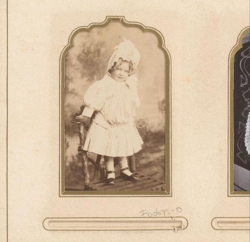 Portrait of a girl in a white dress and cap, standing on a chair