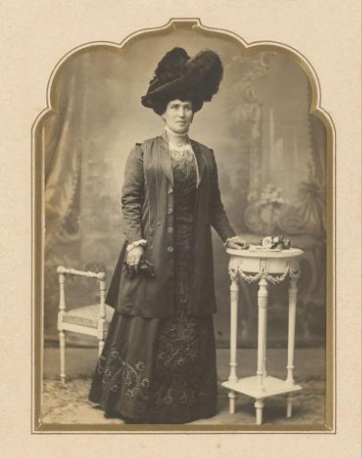 Portrait of a standing woman with a hat and gloves by a table