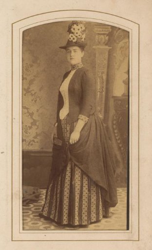 Portrait of a standing woman with a high hat with flowers, fan and overskirt