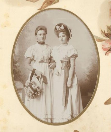 Portrait of two standing girls with flower hats and bows around Empire costumes