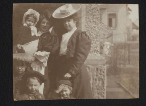 Group portrait of two women and four children in front of a house