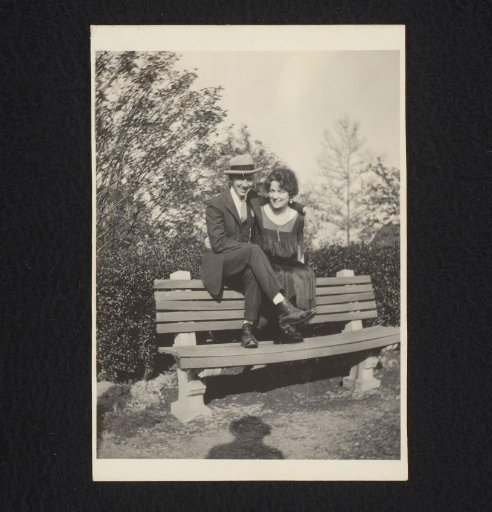 Portrait of a man with a hat and a woman, sitting on the back of a bench in a park