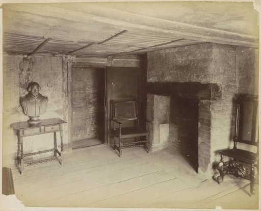 Interior of an old house with a portrait bust, fireplace, chairs and graffiti, probably in England