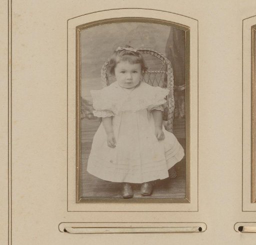 Portrait of a girl standing before a small wicker chair
