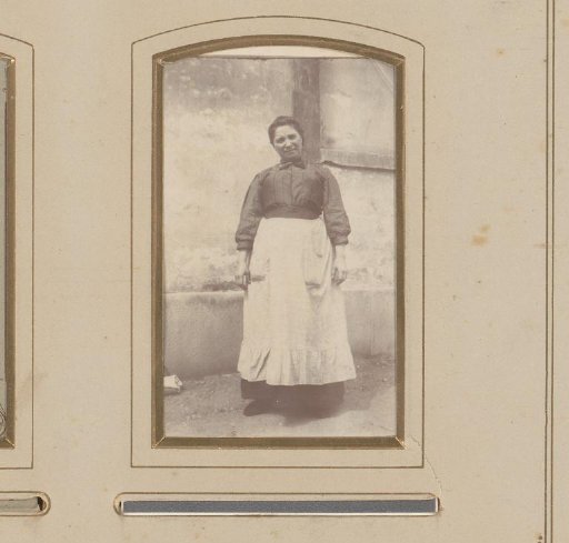 Portrait of a woman with an apron standing before a building