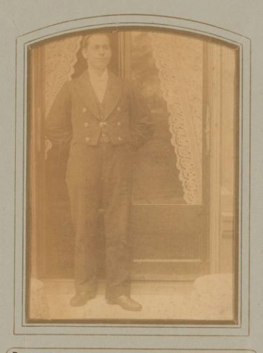 Portrait of an unknown man standing before two doors with lace curtains