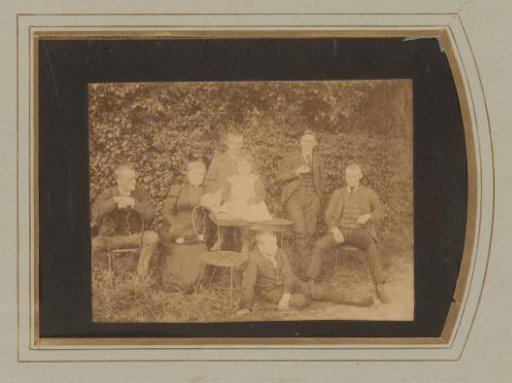 Group portrait of four men, a woman, a boy and a girl, seated around a table in a garden
