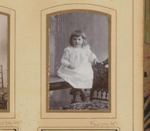 Portrait of a seated girl in a white dress on a table beside a chair