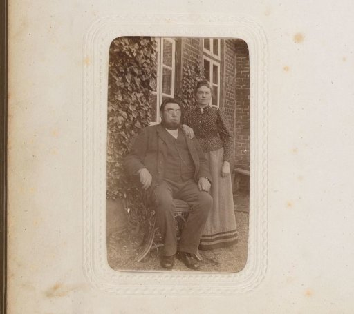 Portrait of a standing woman and a seated man in front of a house