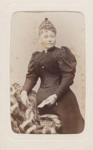 Portrait of a woman standing by a chair, holding a card