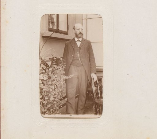 Portrait of a man standing by a chair in front of a house