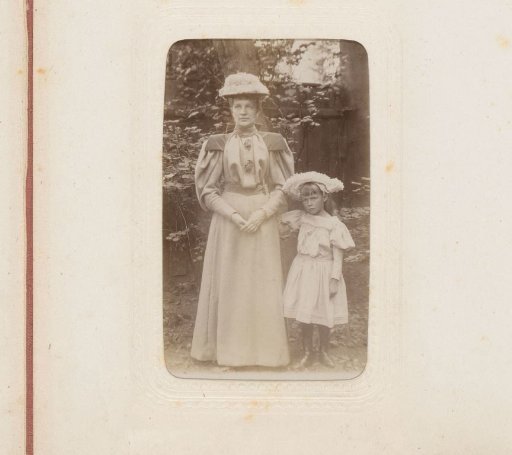 Portrait of a woman and a girl standing in a garden, both wearing hats