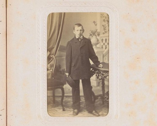 Portrait of a standing young man by a table, holding a hat
