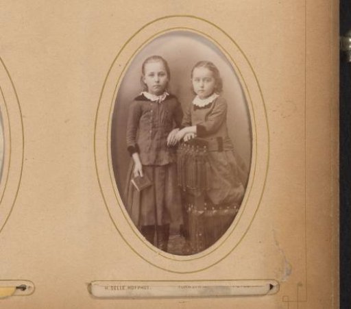 Portrait of two girls, one standing with a book in her hand and one kneeling on a prayer stool