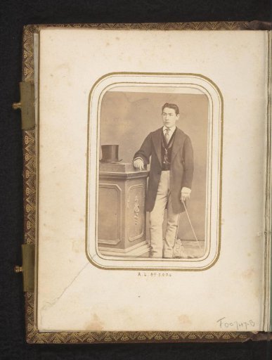 Portrait of a standing young man with a walking stick near a pedestal with a top hat on it