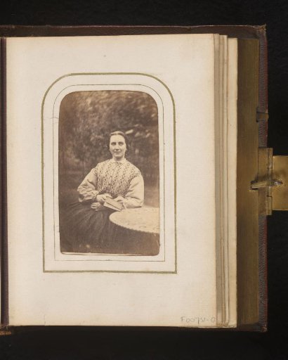 Portrait of a seated woman with a book at a table in a garden