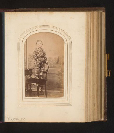 Portrait of a boy in a checkered suit, standing on a chair