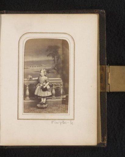 Portrait of a girl with a doll, standing by a balustrade