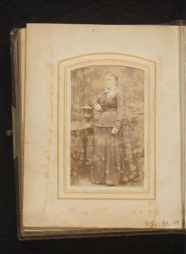 Portrait of a standing woman, leaning on a vase on a table