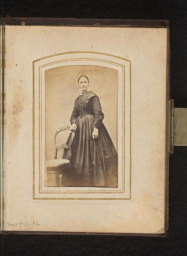 Portrait of a woman with a white cap, standing by a chair