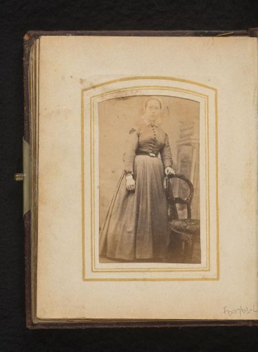Portrait of a woman with a costume cap, standing by a chair