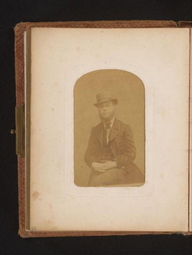 Portrait of a seated bearded man with a hat