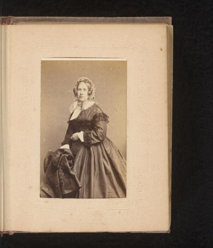 Portrait of a woman with cap, standing by a chair