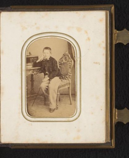 Portrait of a boy seated on a chair with a walking stick