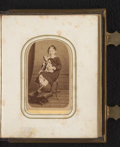 Portrait of a girl seated on a chair, holding a doll