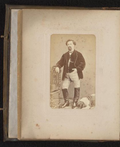 Portrait of a man, standing by a chair with a hat, with a lying dog at his feet