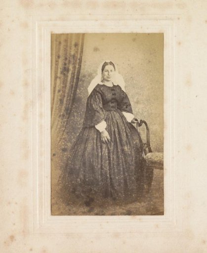 Portrait of a woman with ringlet curls, checkered dress and three-quarter coat, standing