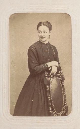 Portrait of a woman in a long dress, standing against a chair back