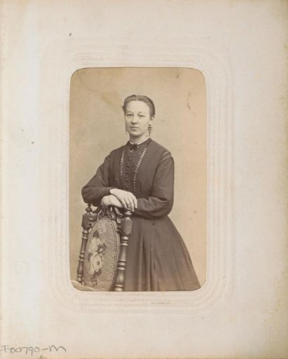 Portrait of a woman in a long dress, standing against a chair back