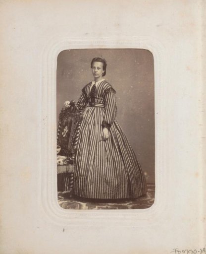 Portrait of a woman in a striped long dress, standing by a chair