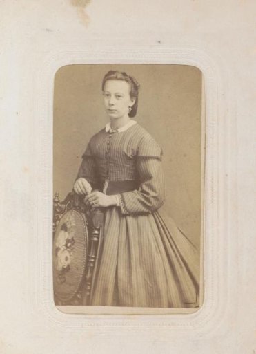 Portrait of a woman in a striped long dress, standing by a chair