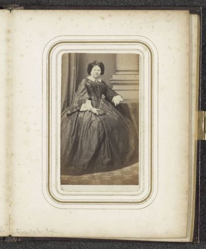Portrait of a woman in a dress and a cap, seated at a table with a book in her hand