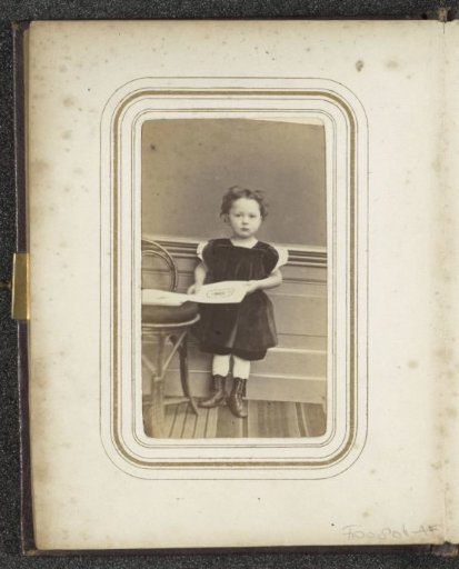 Portrait of a child in a dress, standing by a table with papers in her hands