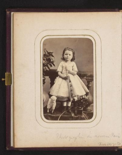 Portrait of a standing girl with shovel, toy sheep and sun hat