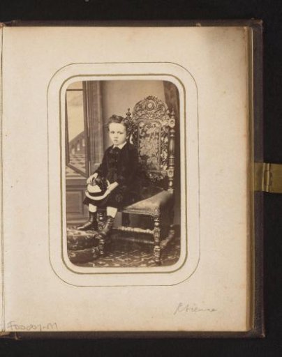 Portrait of a boy with a hat in his hand, sitting on a chair