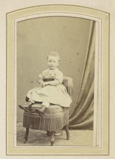 Portrait of a girl in a dress with a sash on an armchair