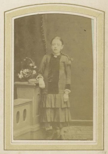 Portrait of a Young Girl with a Pleated Skirt and Blouse by a Flower Basket